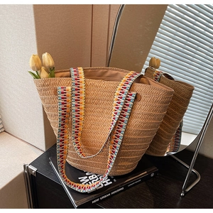 Detail of woven straw tote bag featuring a colorful geometric embroidered shoulder strap