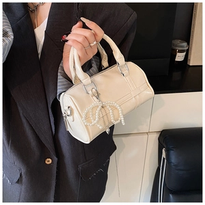 Detail of beige cylinder Boston bag with glossy faux leather and pearl bow charm