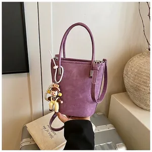 Dettaglio della borsa a secchiello viola con testo a sbalzo e ciondolo a forma di bambola