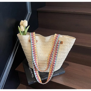 Detail of hand-woven straw tote bag featuring a vibrant multi-color ethnic shoulder strap