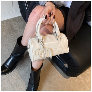 Detail of cream white pillow bag featuring a pearl bow charm and glossy leather finish