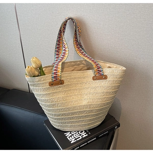 Detail of hand-woven straw bag with colorful Bohemian handle and leather reinforcement