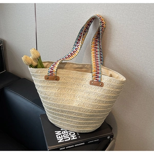 Detail of woven straw tote bag with colorful boho shoulder strap on minimal background