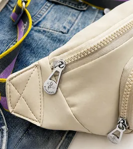 Detailed macro of a textured resin zipper with engraved floral silver puller on a beige bag