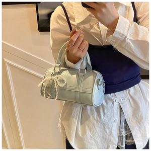 Close-up of light blue pillow bag featuring a pearl bow pendant and dual top handles