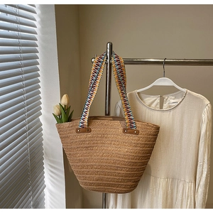 Detail view of a woven straw tote bag with colorful geometric striped fabric straps