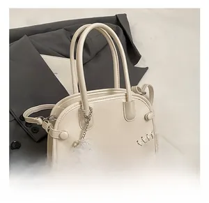 Détail d'un sac en cuir crème avec breloques perles et dentelle sur veste grise