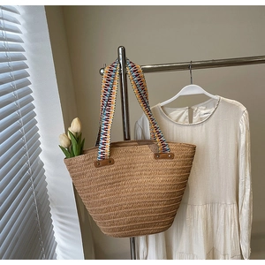 Close-up of a woven straw tote bag featuring a colorful geometric patterned shoulder strap