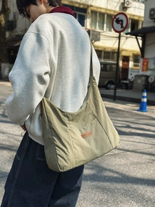 Detail view of khaki green nylon messenger bag with branded leather patch on male model