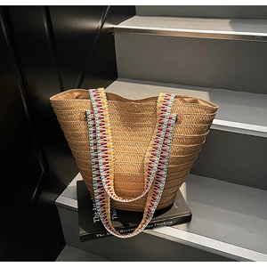 Detail of woven straw tote bag featuring a colorful bohemian style embroidered wide strap