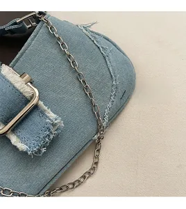 Detail of light blue denim shoulder bag featuring silver metal chain and frayed edges