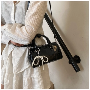 Detail of black glossy pillow bag with pearl bow charm worn with a white textured dress