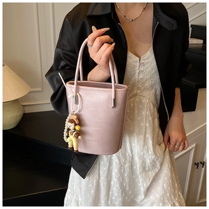 Gedetailleerd zicht op roze lederen emmertas met parelketting en cartoon-hanger accessoire
