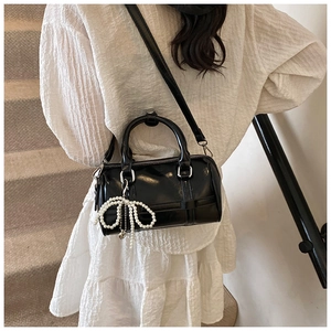 Detail of black glossy pillow bag featuring pearl bow charm on a stylish shoulder strap