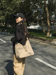 Detail of khaki canvas tote bag with leather logo patch showing large side capacity