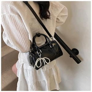 Detail of black glossy leather pillow bag featuring a pearl bow and silver hardware