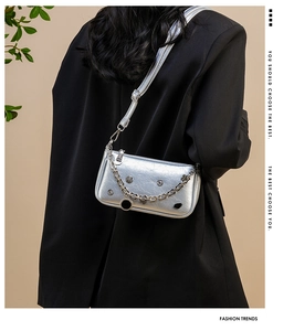 Close-up of a silver metallic crescent bag with chain detail on a model's shoulder
