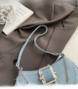 Detail of light blue denim shoulder bag with frayed edges and silver square buckle