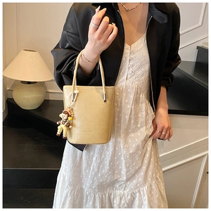 Detail van beige leren emmertas met FASHION & BAGS tekst en schattige clown hanger