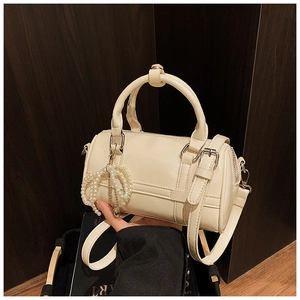 Detail of cream pillow bag with glossy finish and elegant pearl charm on leather handle