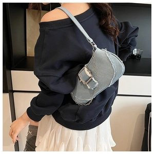 Detail of light blue denim saddle bag featuring distressed edges and a large metal buckle