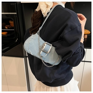 Detail of light blue denim underarm bag featuring fringe edges and metal buckle strap