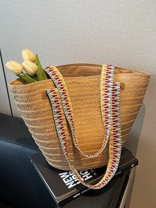 Handwoven straw tote bag with colorful geometric straps and fresh tulips for beach vacation