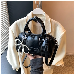 Detail of a black glossy leather cylinder bag featuring a pearl bow charm and silver hardware