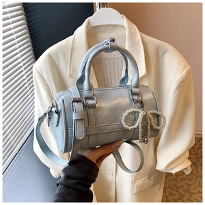Detail of light blue cylinder bag with metal buckles and pearl bow charm accessory