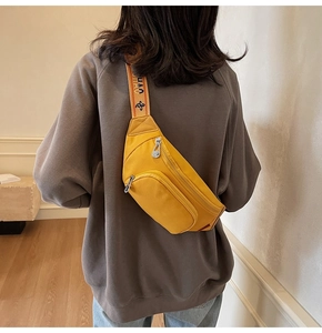 Detail of a bright yellow chest bag featuring an orange jacquard strap with CHAO lettering
