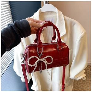 Detail of red glossy pillow bag featuring pearl bow charm and adjustable strap