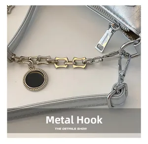 Detail of silver crescent bag featuring polished metal hook, zipper and chain charm