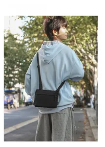 Male model wearing lightweight black nylon crossbody bag in natural outdoor street setting