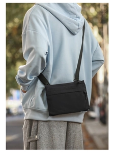 Close-up of black nylon shoulder bag with adjustable strap and zipper detail on model