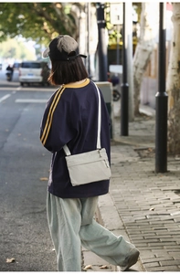 Outdoor street view of a beige lightweight nylon crossbody bag with front zipper pocket