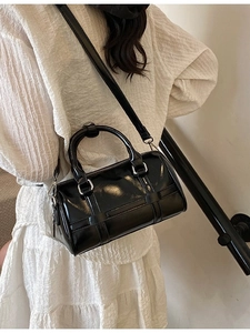 Glossy black pillow bag with dual handles and slim strap worn with white dress