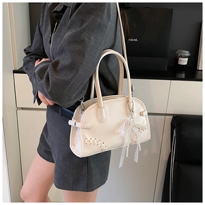 Détail du sac Boston crème avec coutures tressées et breloque perle sur l'épaule