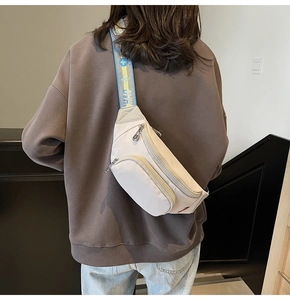 Detail of beige nylon crossbody chest bag with blue patterned strap worn on back