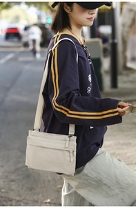 Detail of cream nylon crossbody bag with multiple zippers and wide fabric shoulder strap