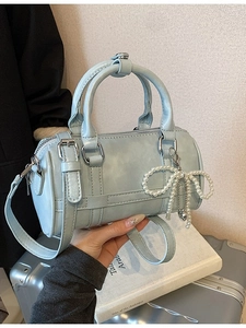 Light blue cylindrical pillow bag with pearl bow pendant shown in a stylish lifestyle setting