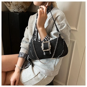 Detail of black denim underarm bag featuring distressed edges and a metallic buckle