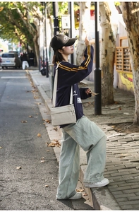 Outdoor street view of a beige nylon crossbody bag shown in a casual lifestyle setting