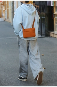 Outdoor shot of a bright orange nylon crossbody bag with adjustable strap on a model