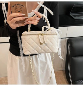 Close-up of white quilted mini box bag with gold chain and lace bow detail