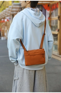 Outdoor shot of a lightweight orange nylon crossbody bag with adjustable strap and zippers