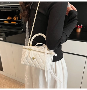 Detailed view of a white quilted box bag with lace bow and chain strap on a model
