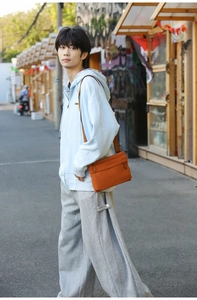 Orange nylon crossbody bag paired with light blue hoodie and casual grey trousers