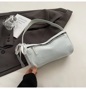 Detail of light blue denim baguette bag with white lace trim and bow on a blazer