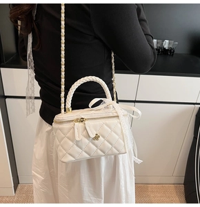Detail of white quilted vanity bag with gold flower charm and woven handle texture
