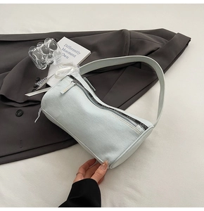 Detail of light blue denim baguette bag with lettered ribbon zipper on grey blazer background